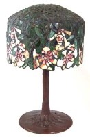 Lot 537 - Tiffany style electric table lamp with a leaded coloured glass shade of leaves and flowers on a patinated naturalistic stem. 72cm high